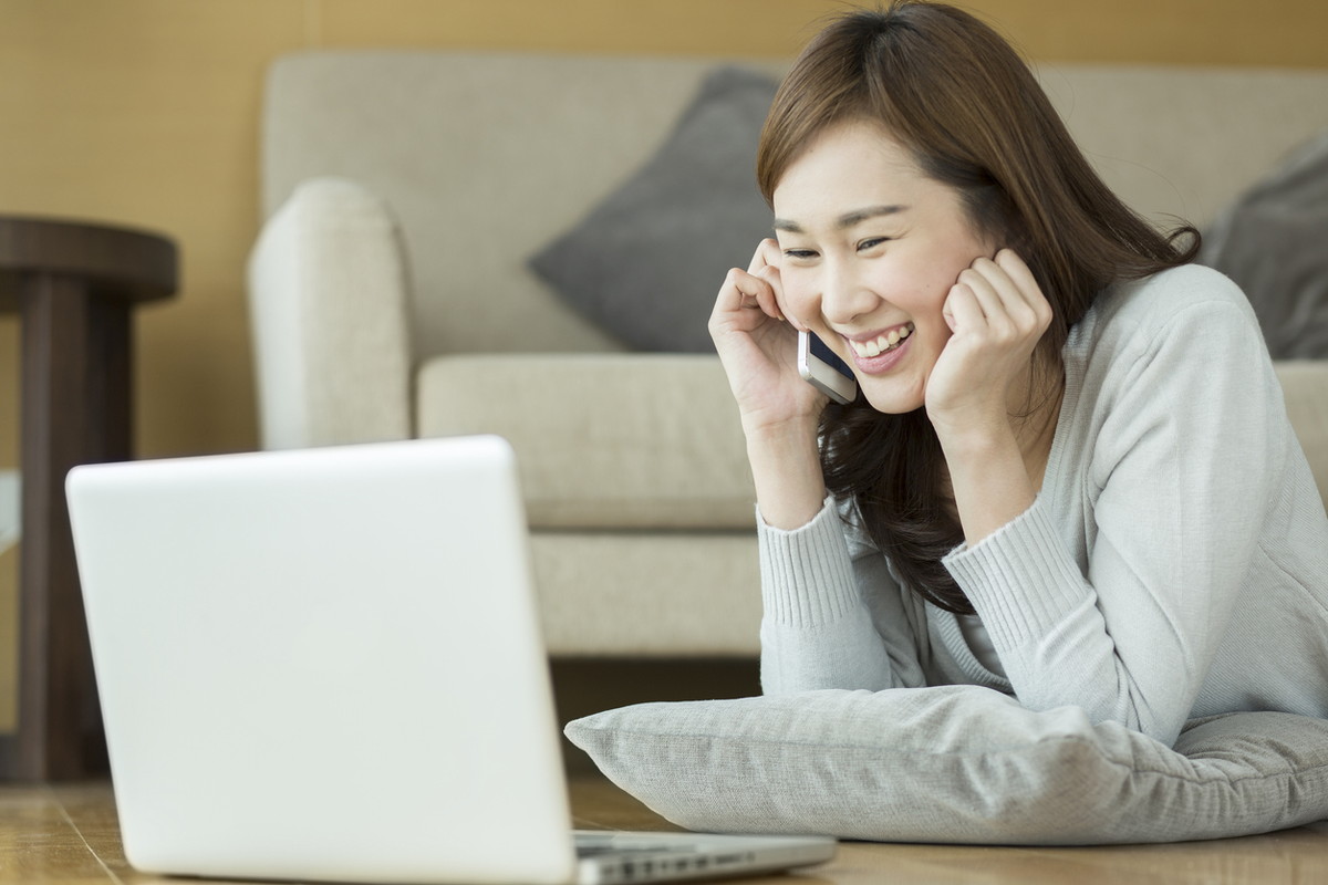 パソコンの前で電話する女性